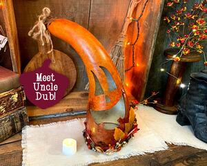 A handcrafted pumpkin gourd named Uncle Dub. It is a tall gourd leaning towards the left decorated with fall leaves and dried berries.